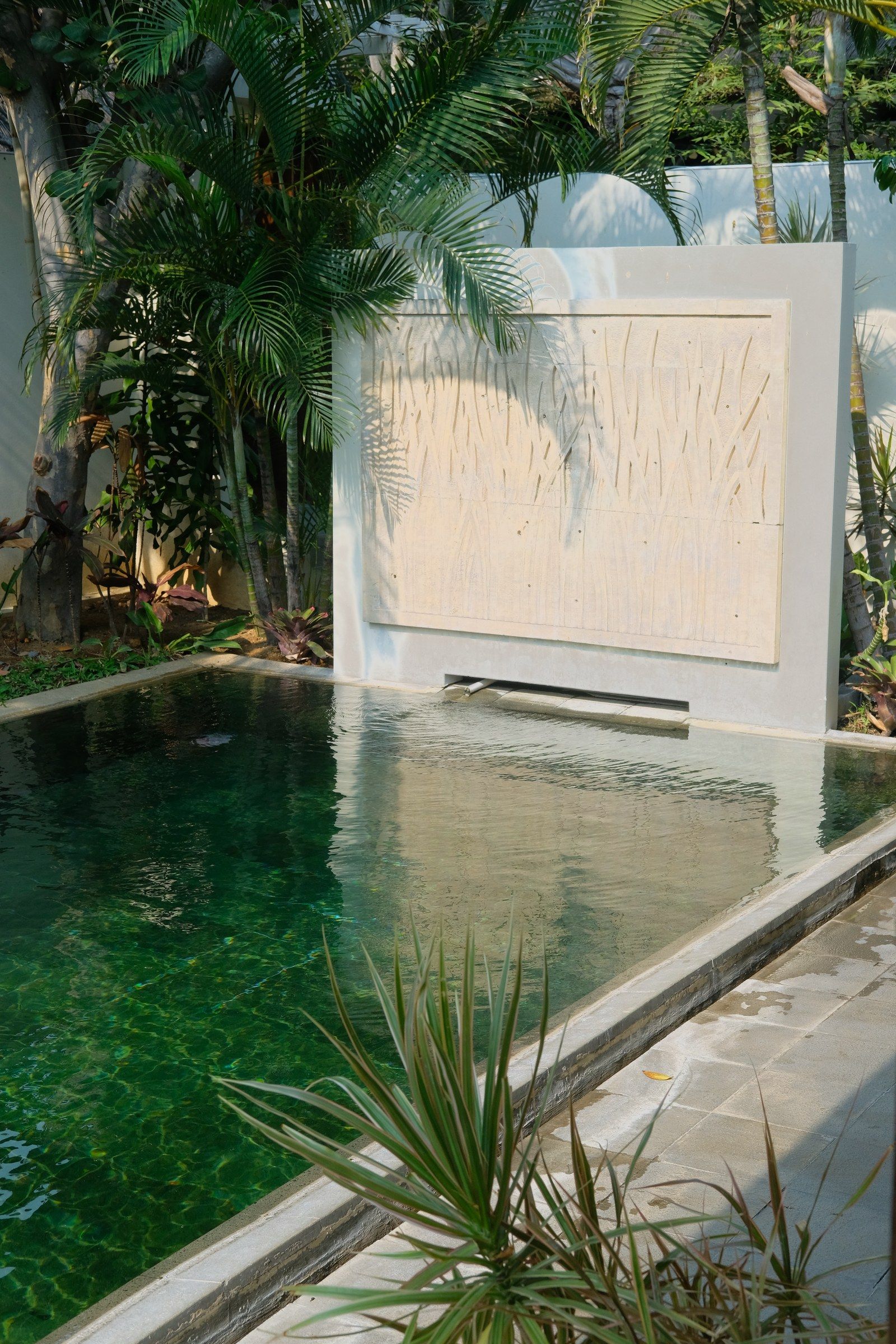 A private hot spring pool in a Sibentang villa yard, with a carved stone panel and palms behind it.